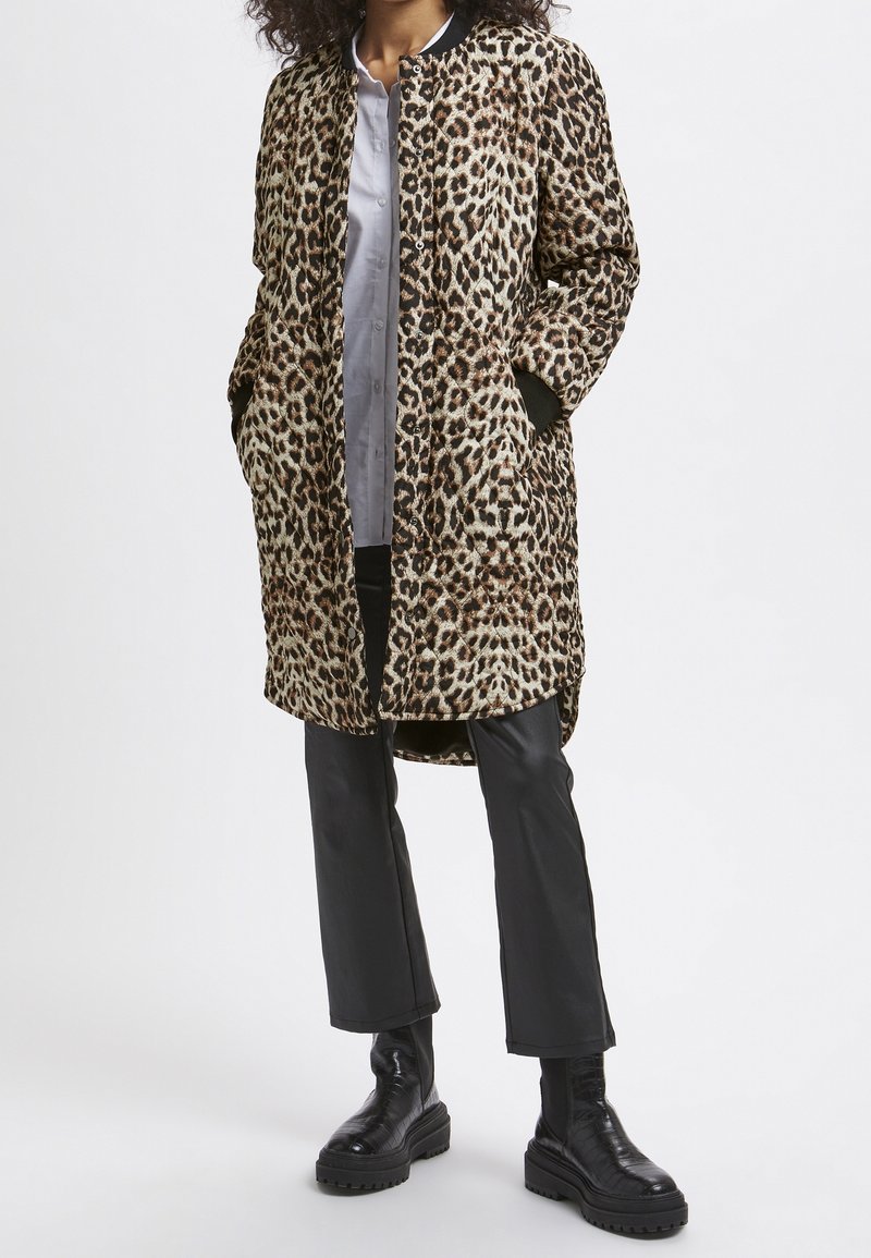 Leopardmønstret frakke med en afslappet pasform, der har to sidelommer, sorte ribbede manchetter og knaplukning. Båret over en lys skjorte og bukser.