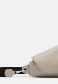 Beżowa skórzana torba z klapką i czarnym regulowanym paskiem. Posiada metalowe okucia oraz gładką, matową teksturę.