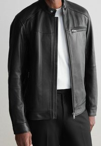 Schwarze Lederjacke mit hohem Kragen, Reißverschluss und aufgesetzter Brusttasche mit Reißverschluss. Sie zeichnet sich durch eine glatte Textur und eine taillierte Passform aus.