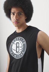 Camiseta sin mangas negra con un gráfico circular que incluye el texto "BROOKLYN" y "NEW YORK", combinado con un motivo de baloncesto.