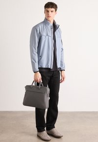 Light blue zip-up jacket with a high collar, paired with a black shirt, dark trousers, gray sneakers, and a gray structured handbag.