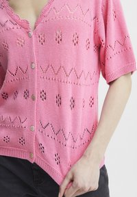 Ružový pletený kardigán s krátkymi rukávmi, s čipkovými vzormi a gombíkovým zapínaním vpredu. Mäkká textúra a voľný strih.