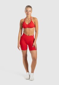 Conjunto de sujetador deportivo rojo y shorts hecho de una tela elástica. El sujetador cuenta con tirantes finos y un detalle fruncido. Los shorts son de tiro alto con un acabado suave.