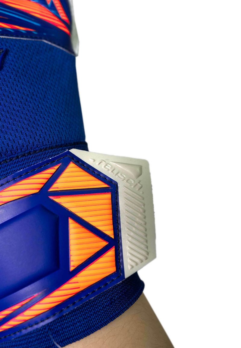 Blue and orange goalkeeper glove strap tightening around wrist, with textured white plastic tab and mesh fabric.