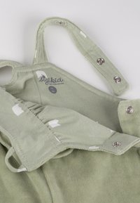 Green baby romper with snap button straps, white patterns, and size label “62 3M” inside neckline.
