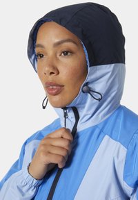 Blauwe en lichtblauwe windbreaker met capuchon, ritssluiting en verstelbare trekkoorden. Voorzien van elastische manchetten en een gladde, waterbestendige textuur.