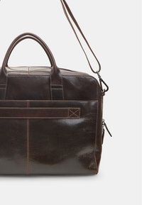 Brown leather briefcase with double handles, adjustable shoulder strap, a front pocket with a stitching detail, and a glossy finish.