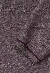 Gestrickter Pullover in tiefem Lila mit strukturierter Oberfläche, ausgestattet mit einem umschlagenen Ärmel und einem kontrastierenden Streifen entlang der Kante.