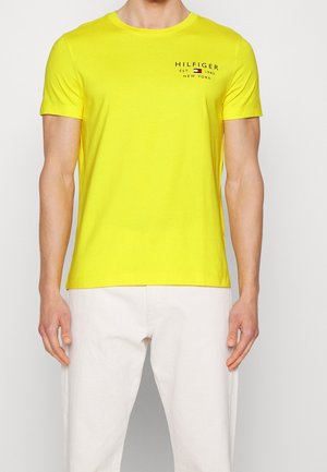 T-shirt en coton jaune à manches courtes, col rond et petit logo avec des accents rouge, blanc et bleu sur la poitrine.