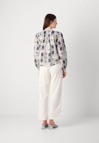 Blusa a maniche lunghe con motivo blu e crema, dettagli plissettati sulla schiena, abbinata a pantaloni a gamba larga crema e sandali trasparenti con tacco a blocco.