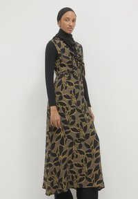 Maxikleid in schwarz mit goldfarbenem Blumenmuster und gebundenem Ausschnitt. Hergestellt aus strukturiertem Stoff, über einem Langarmoberteil und einer Hose geschichtet.