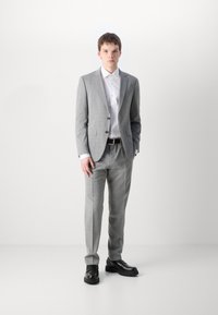 Completo grigio chiaro con finitura strutturata, camicia bianca con colletto, cintura nera e scarpe nere. Vestibilità sagomata, che mette in evidenza un design moderno.