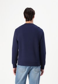 Navy blue sweatshirt with a crew neckline, ribbed cuffs, and hem; made from a soft fabric with a smooth texture. Worn with light blue jeans.