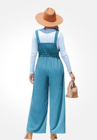 Teal wijde jumpsuit met verstelbare banden en elastische taille. Gecombineerd met een beige gevlochten handtas en een hoed met brede rand in lichtbruin.