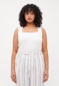 Top blanco sin mangas con un escote cuadrado, combinado con pantalones livianos a rayas en blanco, azul y marrón, con cintura ajustable con cordón.