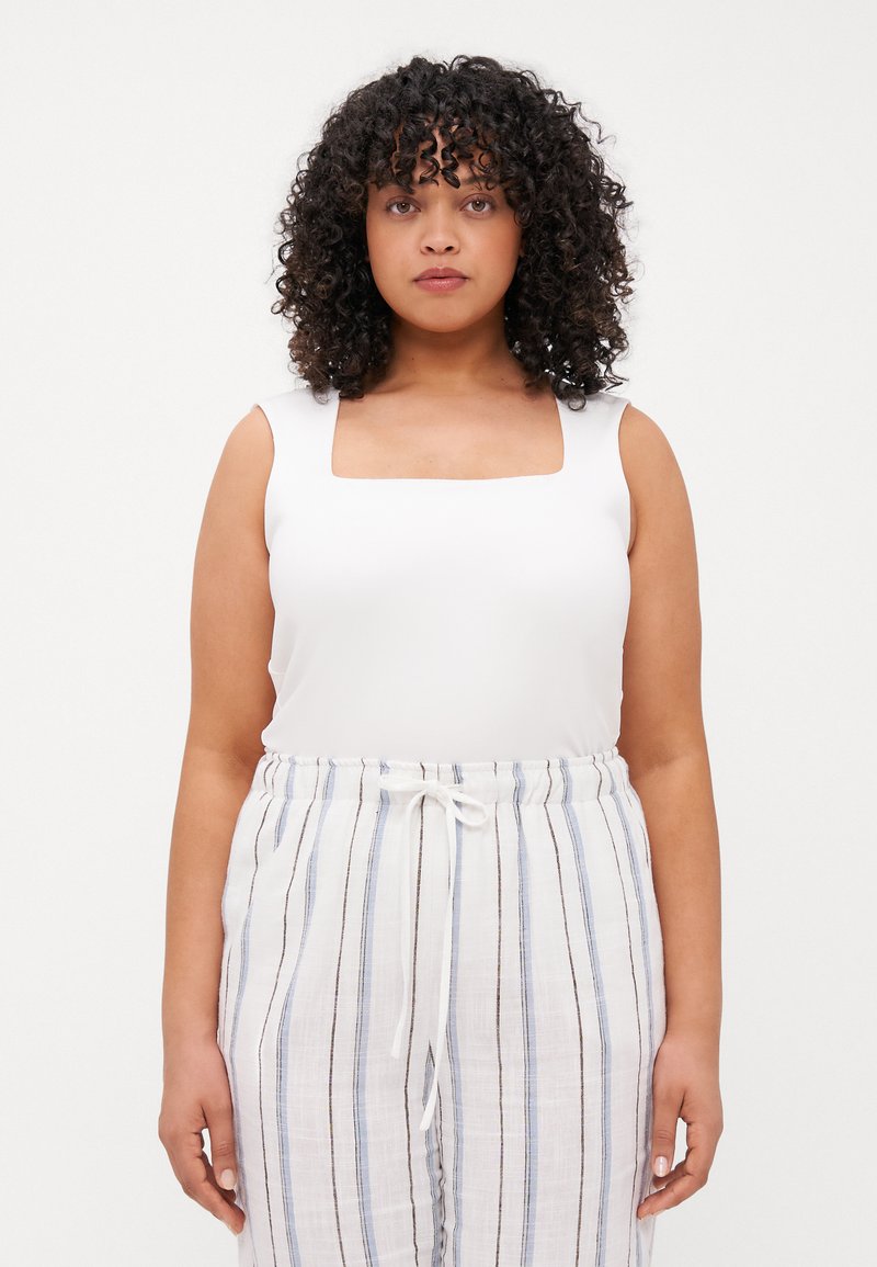 Top blanco sin mangas con un escote cuadrado, combinado con pantalones livianos a rayas en blanco, azul y marrón, con cintura ajustable con cordón.