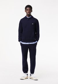 Mörkblå hoodie med framficka, parat med matchande mörkblå joggers. Vit skjortkrage syns under, kompletterad med vita sneakers.