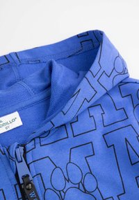 Niebieska bluza z zamkiem, wykonana z miękkiej tkaniny, z czarnym nadrukiem z wyraźnymi literami i wzorami łap. Metka widoczna wewnątrz kołnierza.