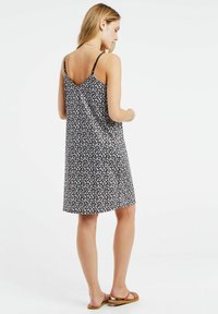 Zwarte jurk met bloemenprint, dunne banden en een V-vormige rugopening. De stof heeft een gladde textuur en is versierd met kleine witte en roze bloemen.