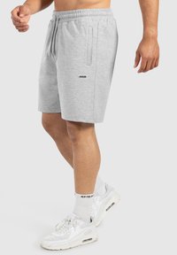 Pantalones cortos elásticos de color gris claro con cintura elástica y bolsillos laterales, hechos de una tela suave, con un pequeño logotipo negro en la parte delantera.