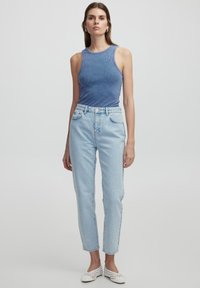 Niebieski prążkowany top bez rękawów w połączeniu z jasnoniebieskimi dżinsami o wysokim stanie. Model nosi białe, fakturowane buty. Prosty, schludny design z minimalnymi akcentami.