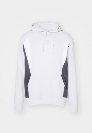 Sudadera blanca con paneles laterales grises, bolsillo canguro, capucha ajustable y un logo sutil en el pecho. Hecha de una suave mezcla de algodón.
