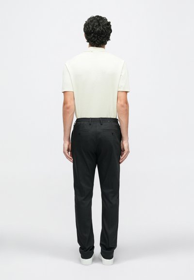 Polo de mangas curtas em bege claro e calças pretas com cintura elástica. Design simples sem padrões visíveis. Ténis brancos.