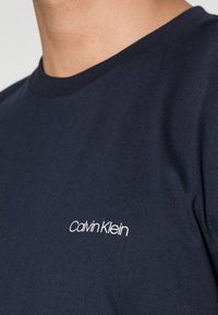 T-shirt in cotone blu navy con scollatura rotonda, caratterizzato da un logo bianco "Calvin Klein" sul petto. Texture liscia, vestibilità casual.