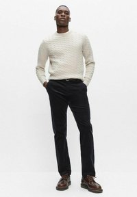 Ljust beige kabelstickad tröja kombinerad med mörk marinblå manchesterbyxor. Bruna snörskor fulländar outfiten. Enkel och modern design.