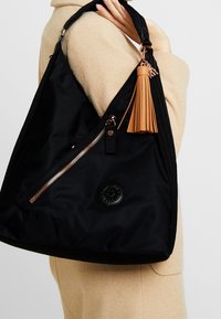 Zwarte nylon handtas met een slouchy ontwerp, met een zijrits, een reliëflogo en een tan leren kwastaccent.