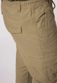 Khaki spodnie cargo w luźnym kroju, z elastycznym paskiem w talii, bocznymi kieszeniami i naszywką z logo na tylnej kieszeni. Gładki materiał bawełniany.