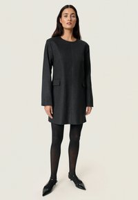 Fekete csíkos ruha hosszú ujjakkal, két oldalsó zsebbel és kerek dekoltázzsal. Fekete, átlátszatlan zoknival és hegyes lapos cipővel párosítva.