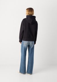 Felpa nera con cappuccio dal taglio rilassato, abbinata a jeans a gamba larga blu chiaro. Texture del tessuto morbida e dettagli di cucitura evidenti.