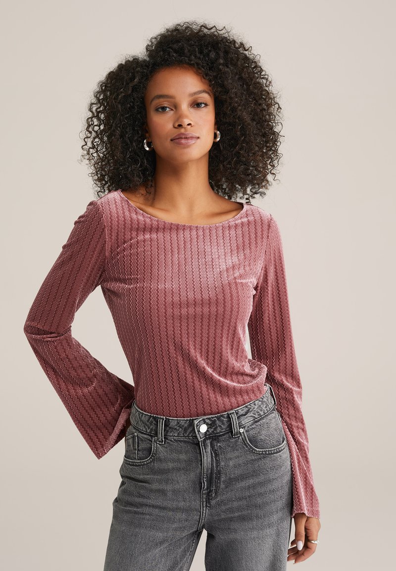 Pikad varrukad, tekstuuriga tipp tolmust roosast värvitoonis, millel on sakiline muster, laia kaeluse ja vabalt langeva lõikega, koos kõrge vöökohtadega hallide teksadega.