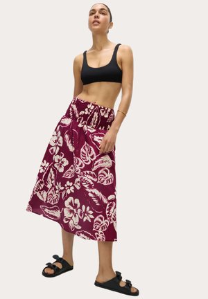 Gonna maxi a stampa floreale bordeaux con vita arricciata, abbinata a un crop top nero a coste e sandali neri scivolati con dettagli a fiocco.