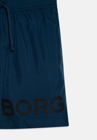 Námornícke modré plavky s elastickým pásom a šnúrkou na sťahovanie. Obsahuje veľké čierne logo "BORG" potlačené na dolnej ľavej strane. Hladká textúra.