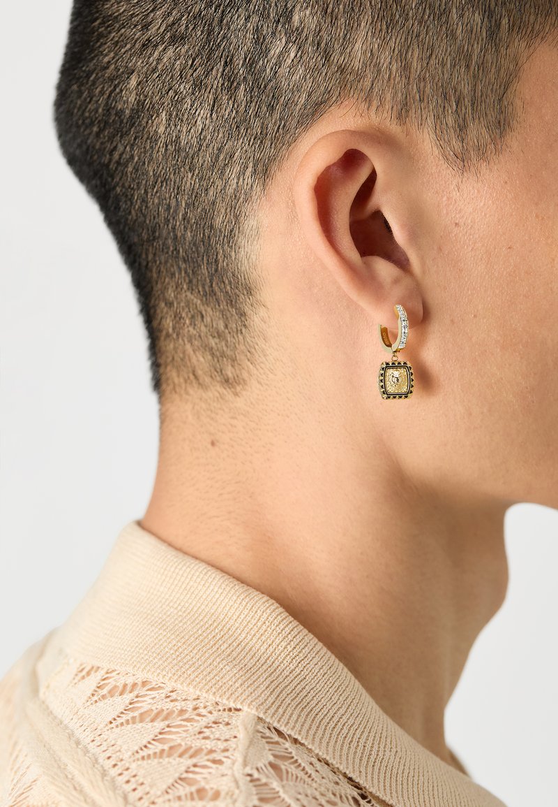 Gold-tone hoop earrings with a square gemstone pendant, embellished with small crystals, showcased on a textured, light sweater.