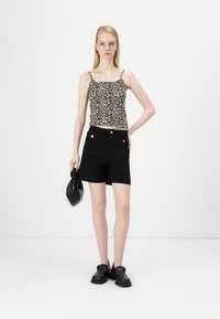 Sorte shorts med gullknappede lommer, paret med en leopardmønstret cami. Modellen holder en teksturert svart håndveske, iført svarte sko.