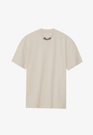 Beige lühikeste varrukatega T-särk, mis on valmistatud pehmest puuvillast, ümar kaelus, millel on musta kiri "Detroit" kaeluse lähedal.