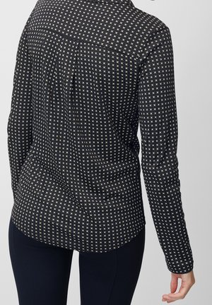 Sort langærmet skjorte med små hvide firkantmønstre båret af en person set bagfra, kombineret med mørke bukser.