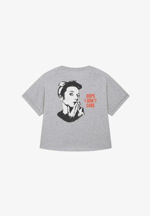 Grijze katoenen t-shirt met een zwarte afbeelding van een vrouw met een hoofddoek en de tekst "OOPS I DON'T CARE" in vet oranje. Korte mouwen, relaxte pasvorm.