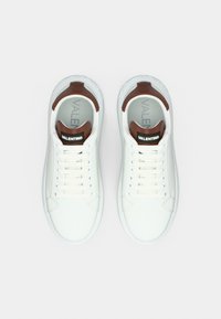 Άσπρα δερμάτινα αθλητικά παπούτσια με λεία επιφάνεια, καφέ λαστιχένιες λεπτομέρειες στη φτέρνα και άσπρα κορδόνια. Το λογότυπο είναι τυπωμένο στη γλώσσα.