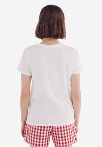 Witte katoenen t-shirt met korte mouwen, losse pasvorm en ronde hals, gecombineerd met rode en witte geruite shorts.