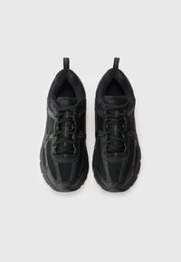 Baskets de sport noires avec une tige en maille respirante, semelle en caoutchouc texturée et fermeture à lacets. Comprend des languettes au talon pour un enfilage facile.