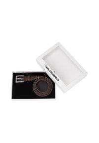 Bruine leren riem met zilverkleurige metalen gesp, gepresenteerd in een witte doos met zwarte binnenbekleding en "KARL LAGERFELD" branding op de deksel.