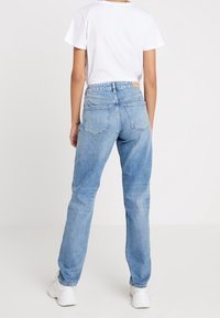 Jeans de mezclilla de color azul claro con un corte relajado, con un diseño de cinco bolsillos y un ligero desgastado. Combinados con una camiseta blanca lisa.