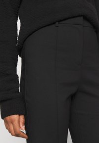 Czarny, teksturowany sweter o miękkim, pluszowym wykończeniu, w połączeniu z dopasowanymi czarnymi spodniami o eleganckim kroju i subtelnych przeszyciach.