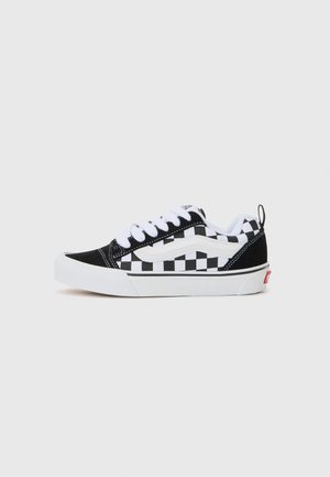 Black and white checkered canvas sneakers with white laces, rubber sole, and padded collar. Features logo accents and contrasting texture.