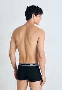 Schwarze Baumwoll-Boxershorts mit grauem elastischem Bund, der das „HUGO“-Logo trägt. Das Modell wird von hinten gezeigt, um Passform und Design zu betonen.