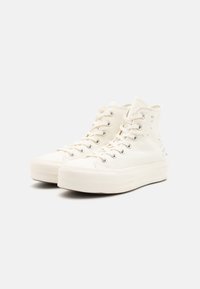 Λευκά ψηλά αθλητικά παπούτσια από καμβά, με στρογγυλή μύτη, μεταλλικά μάτια και διακοσμητικές τρυπήσεις στο πλάι. Παχύ λάστιχο σόλας.